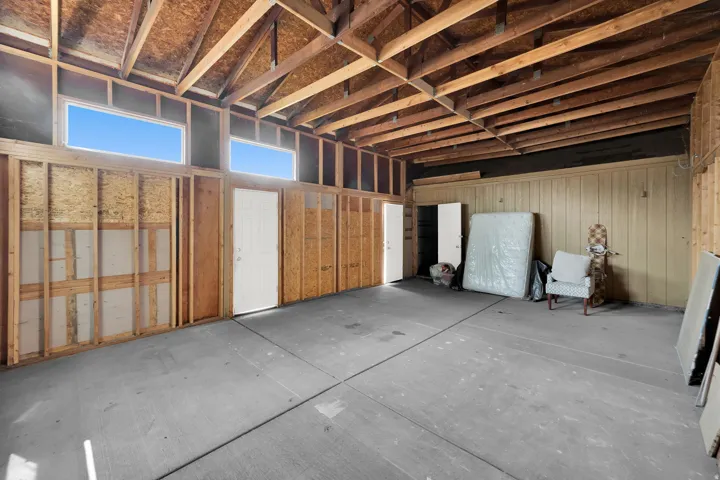 Unfinished interior space featuring exposed wood framing, high ceilings with exposed beams, two transom windows, concrete flooring, and multiple solid panel doors