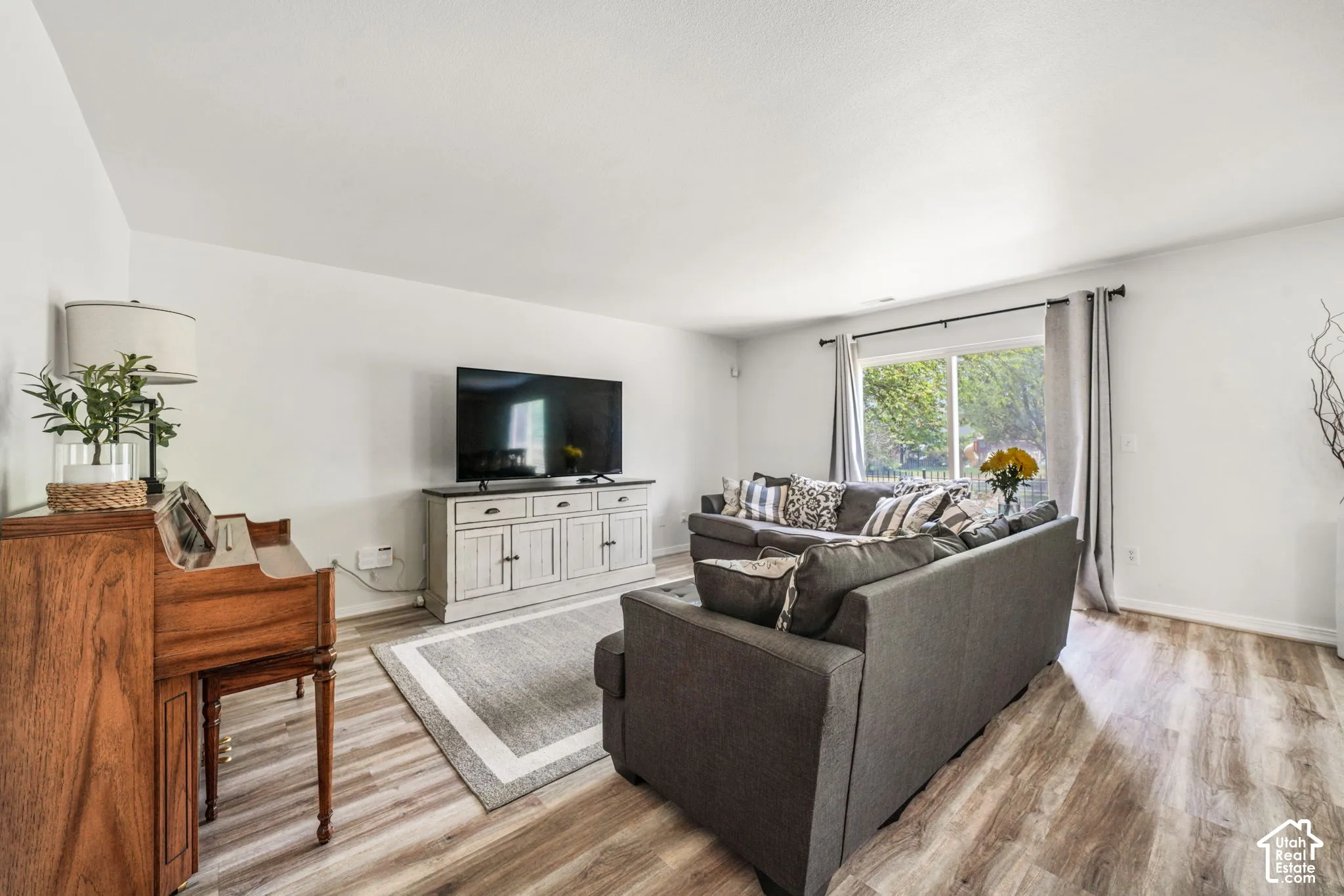 Spacious living area featuring light wood-finish flooring, white walls, and a sliding glass door providing natural light