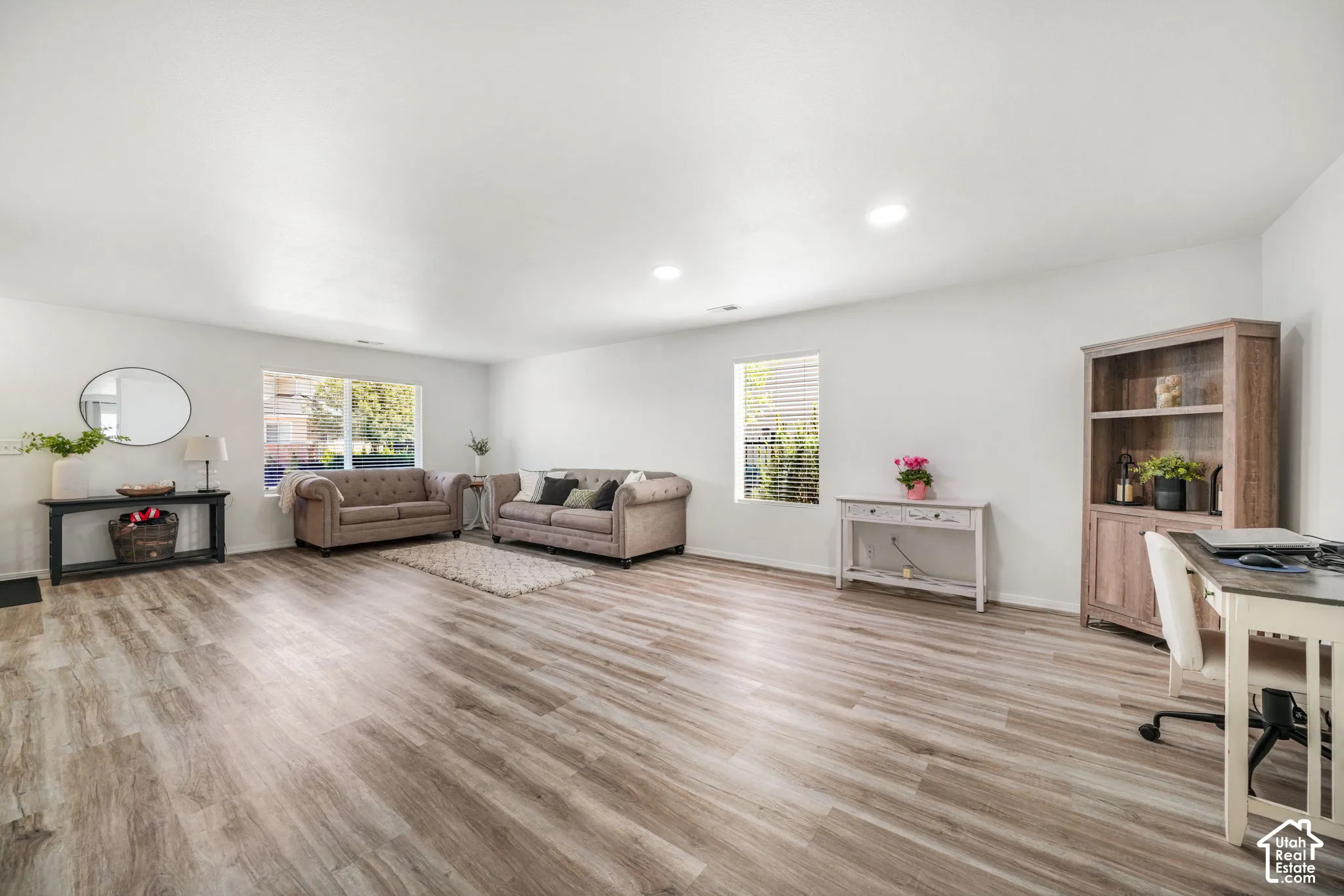 Spacious living area featuring light wood-finish flooring, recessed lighting, and white painted walls
