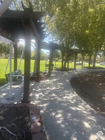 Expansive outdoor area featuring a concrete pathway, multiple pergolas with swings, and mature trees providing shade