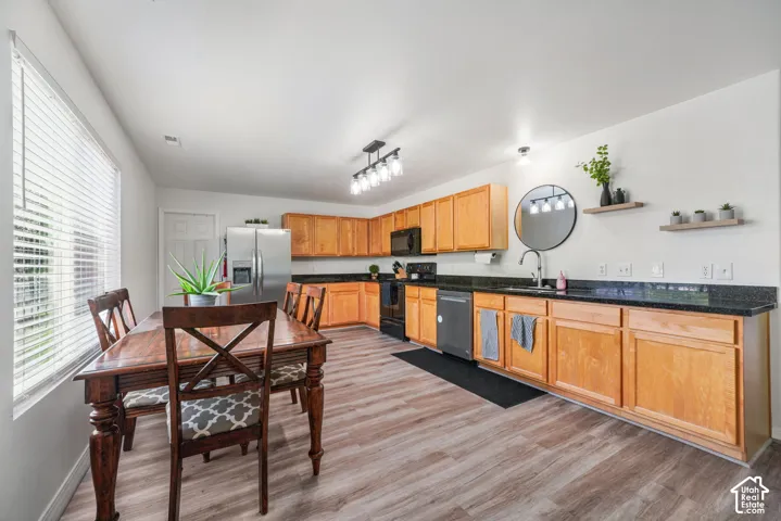 Open-concept kitchen and dining area featuring wood-finish flooring, light wood cabinetry, black countertops, and stainless steel appliances