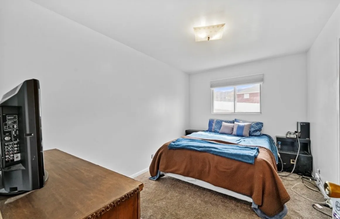 Carpeted bedroom with a single window, white walls, and a ceiling-mounted light fixture