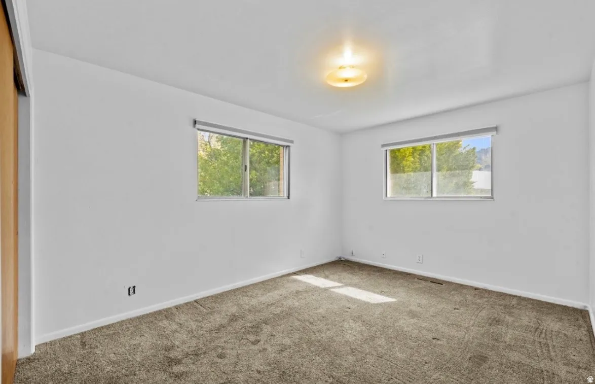 Spacious room featuring neutral carpeting, white walls, and two windows with outdoor scenery
