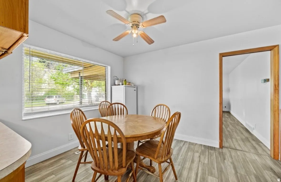 Dining area featuring a wide window with horizontal blinds, wood-finish flooring, and a ceiling fan