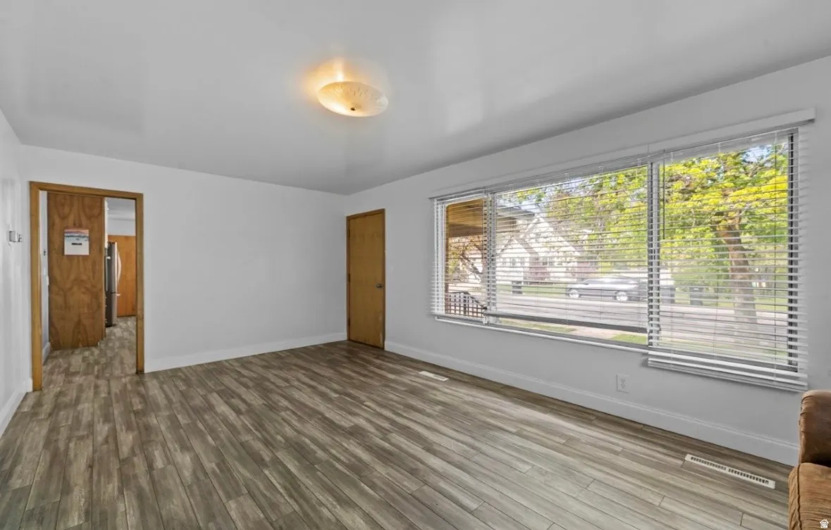 Spacious room featuring wood-finish flooring, white baseboards, and a large window with horizontal blinds