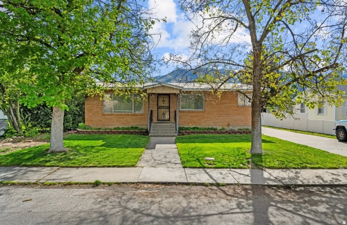 Brick-front residence featuring a covered entry, established landscaping, and a paved driveway