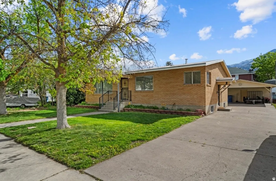 Brick exterior home with a covered front entry, concrete driveway, and a carport