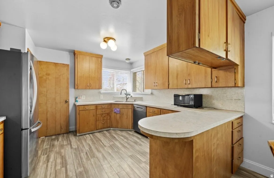 Kitchen featuring wood-finish cabinetry, light countertops, wood-finish flooring, a window with blinds, and a built-in sink