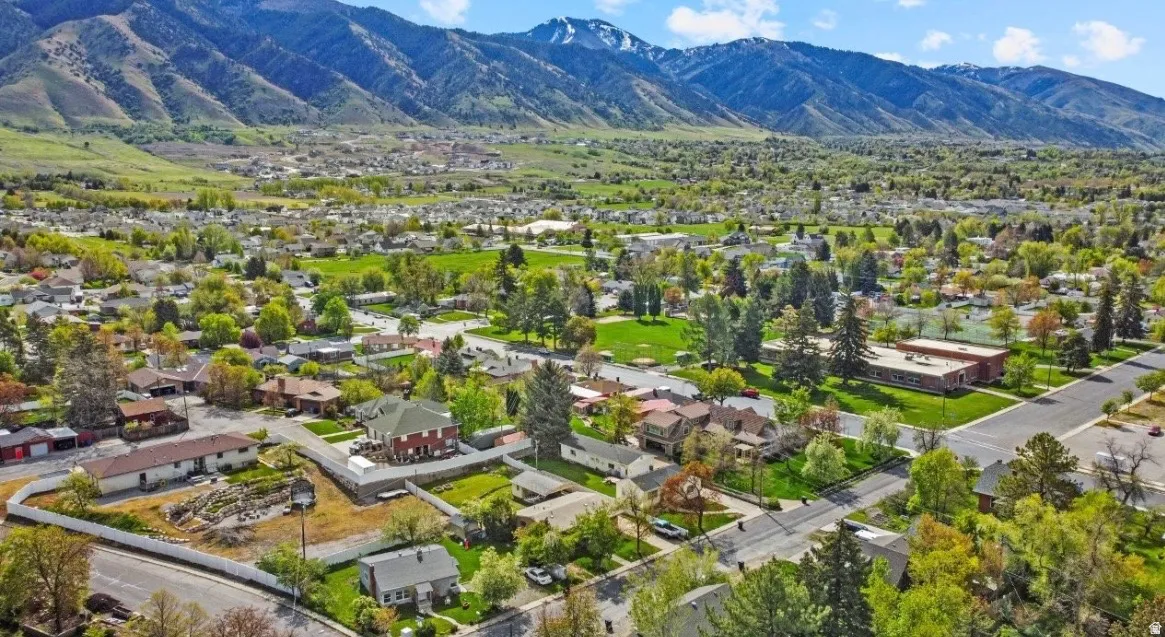 Expansive aerial view of a residential area with varied housing styles, mature trees, and mountainous terrain in the background