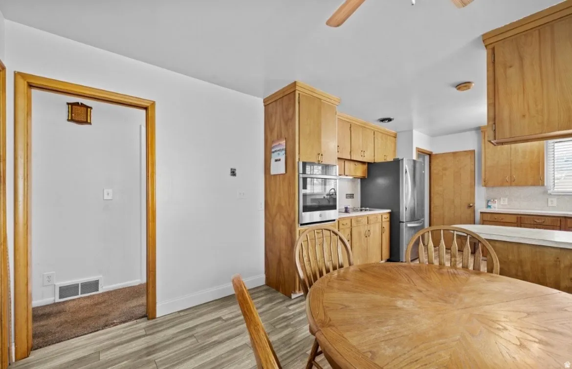 Kitchen area featuring light wood cabinetry, stainless steel refrigerator, built-in oven, and wood-finish flooring