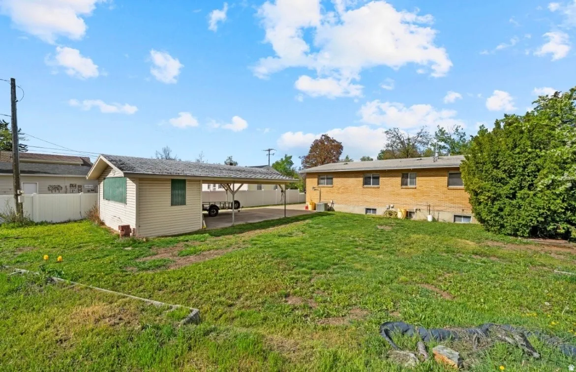 Spacious rear yard featuring an expansive lawn, a detached shed with an attached carport, and a brick-sided structure