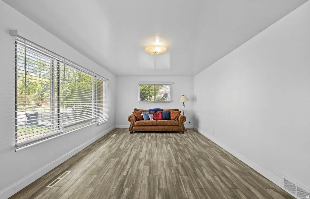 Spacious room featuring wood-finish flooring, white walls, and a large window with blinds