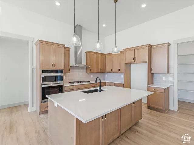 Open-concept kitchen featuring light wood-finish cabinetry, a large center island with a light-toned countertop, stainless steel appliances, and wood-finish flooring