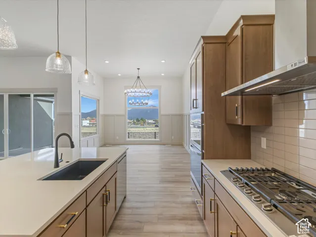 Kitchen featuring wood-finish flooring, light quartz countertops, a gas range with a stainless steel hood, and shaker-style cabinetry with gold-tone hardware