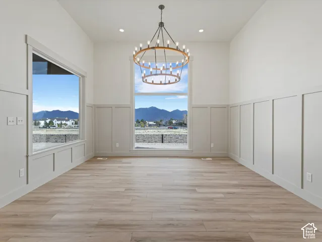 Vaulted ceiling with an overhead chandelier, multiple large windows, wainscoting details, and wood-finish flooring