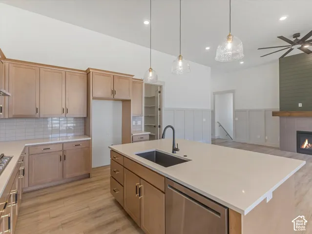 Kitchen with light wood-finish cabinetry, light countertops, subway tile backsplash, and a large island with an undermount sink