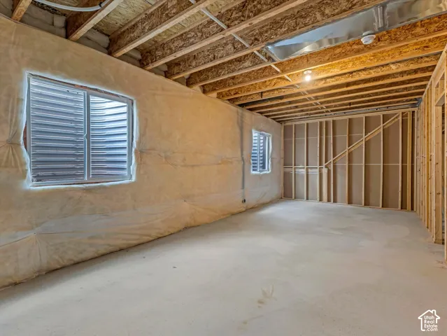 Unfinished basement featuring exposed wood joists, concrete flooring, and two egress windows