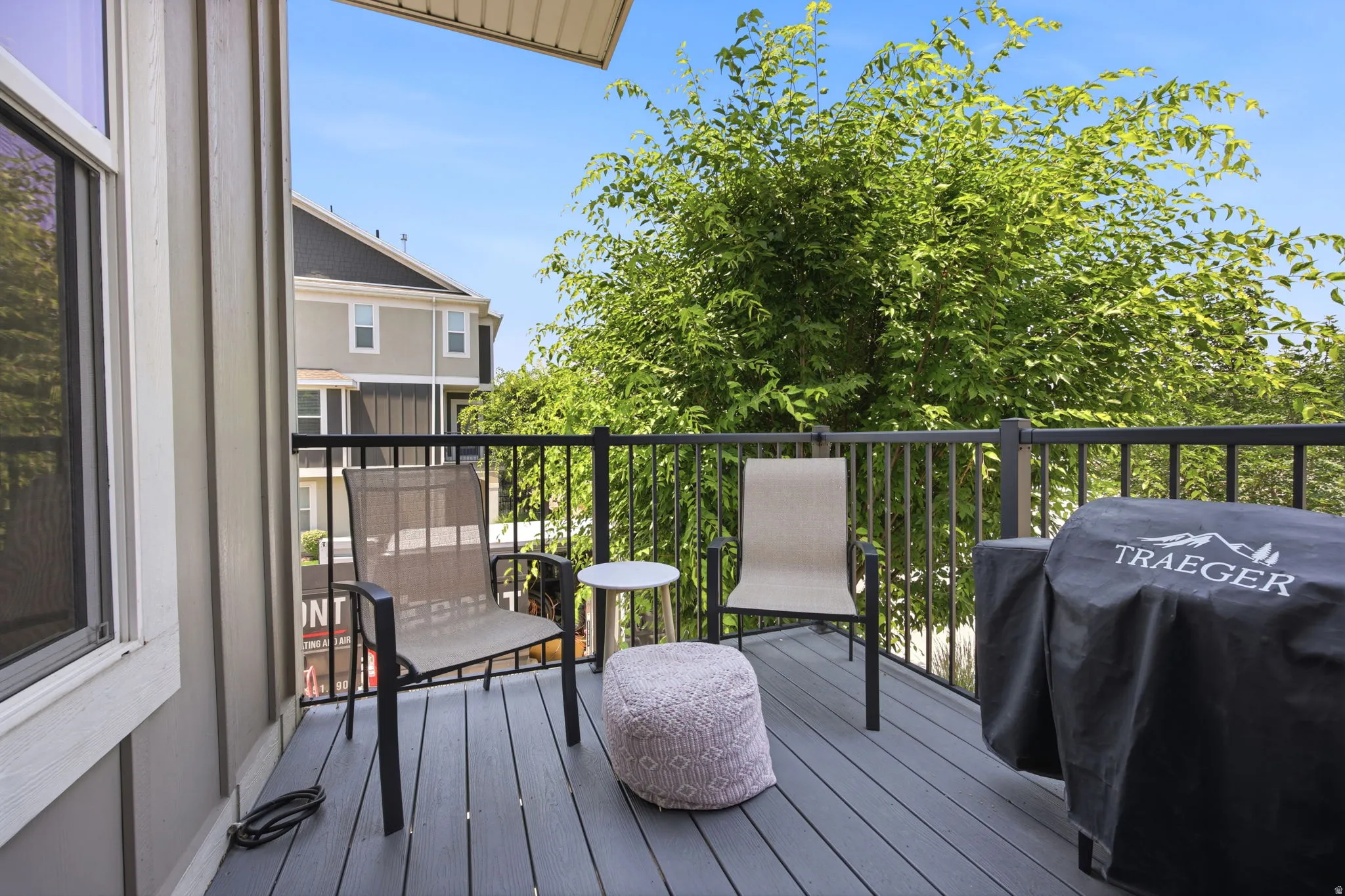 Outdoor deck featuring composite flooring, black metal railings, and a prominent green tree backdrop