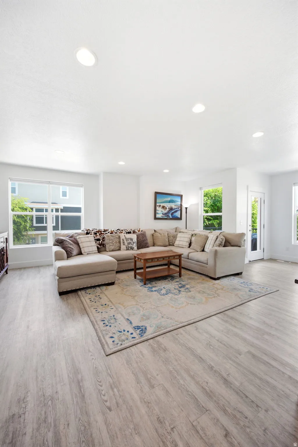 Spacious living area featuring light wood-finish flooring, recessed lighting, and ample natural illumination from multiple windows