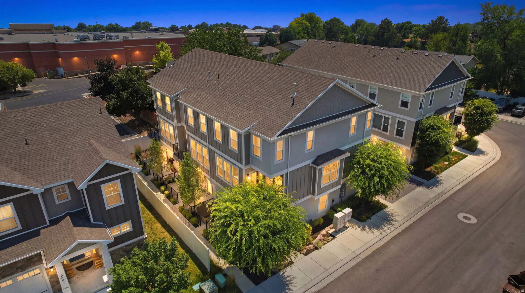 Modern townhome with multi-level architecture, a gray and cream exterior, dark shingle roofing, and a private fenced yard