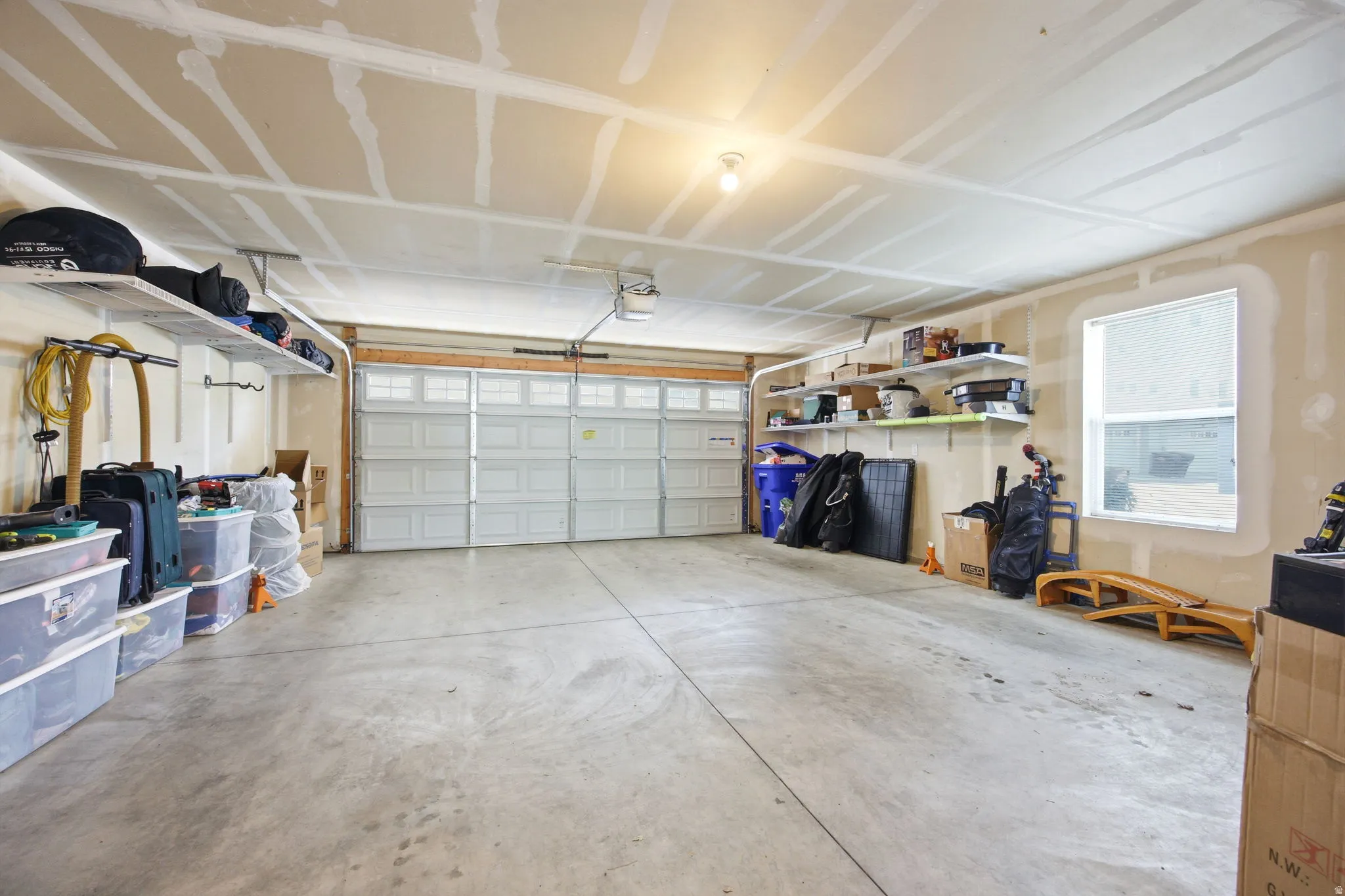 Two-car garage featuring a concrete floor, overhead lighting, an exterior-facing window, and built-in shelving