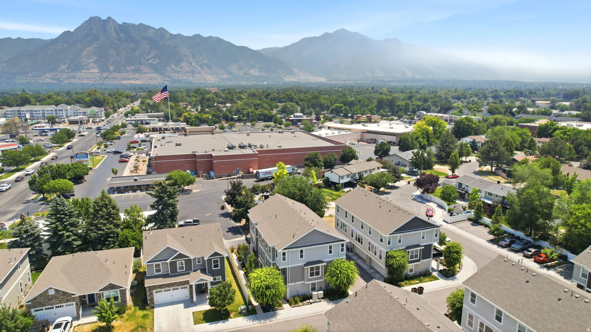 Aerial perspective showcasing multiple residential structures, a commercial building with a large parking area, and a prominent flag pole