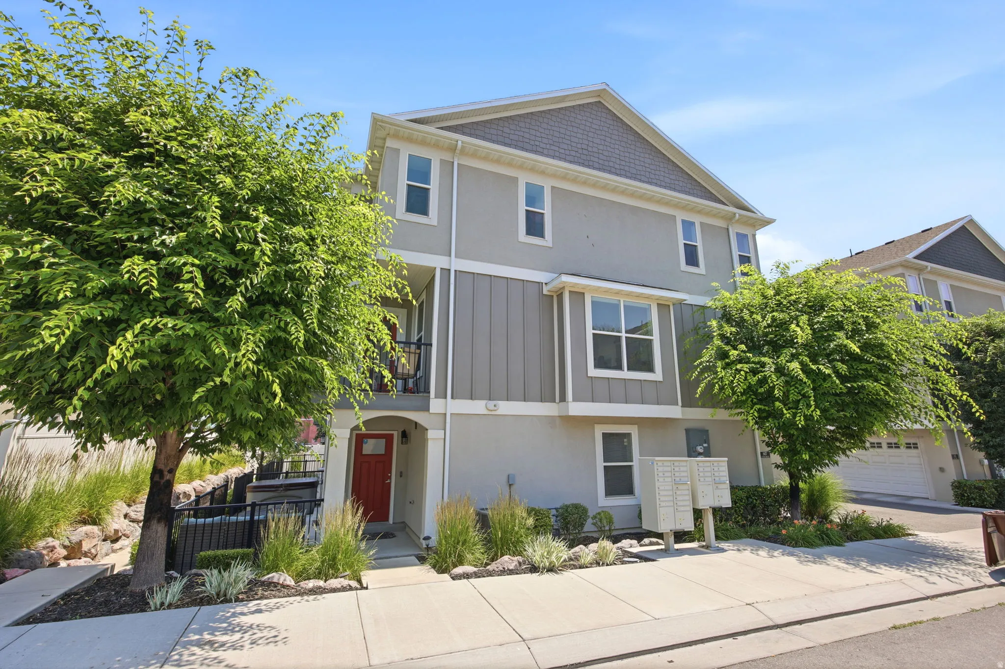 Contemporary multi-story residence featuring a striking red entry door, an upper-level balcony with black railing, and a gabled roofline with shingle siding