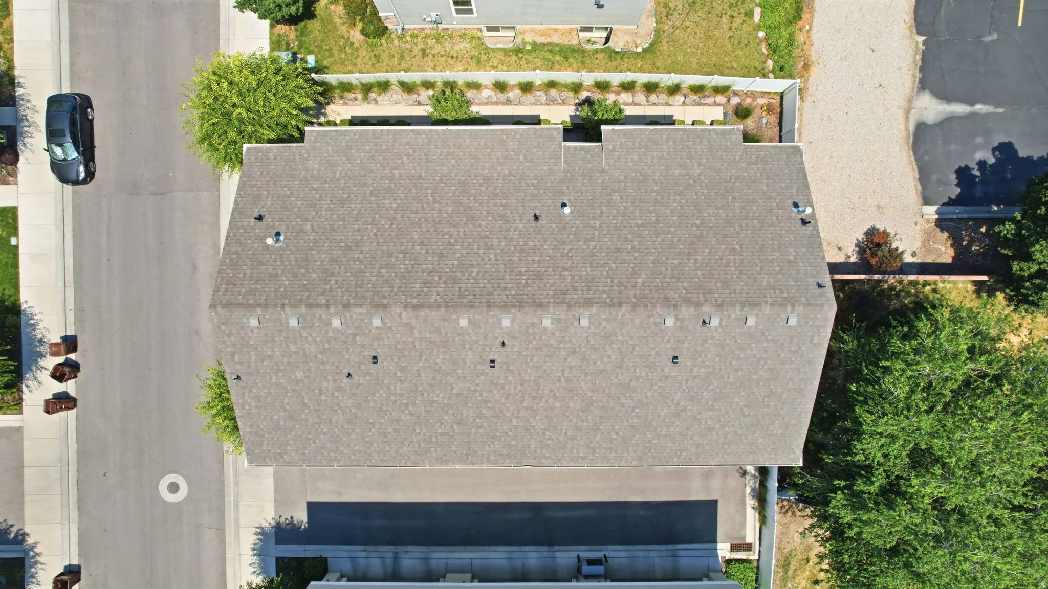 Gable roofline featuring asphalt shingles, multiple roof vents, and a perimeter of mature landscaping