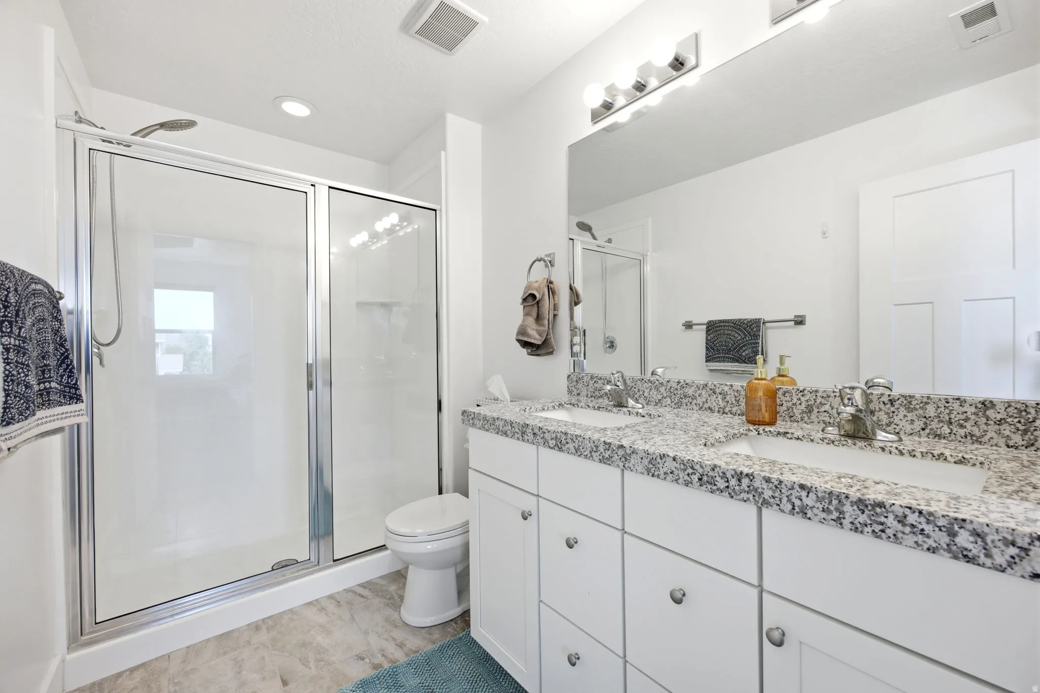 Bright bathroom featuring a dual vanity with a granite-style countertop, white cabinetry, and undermount sinks