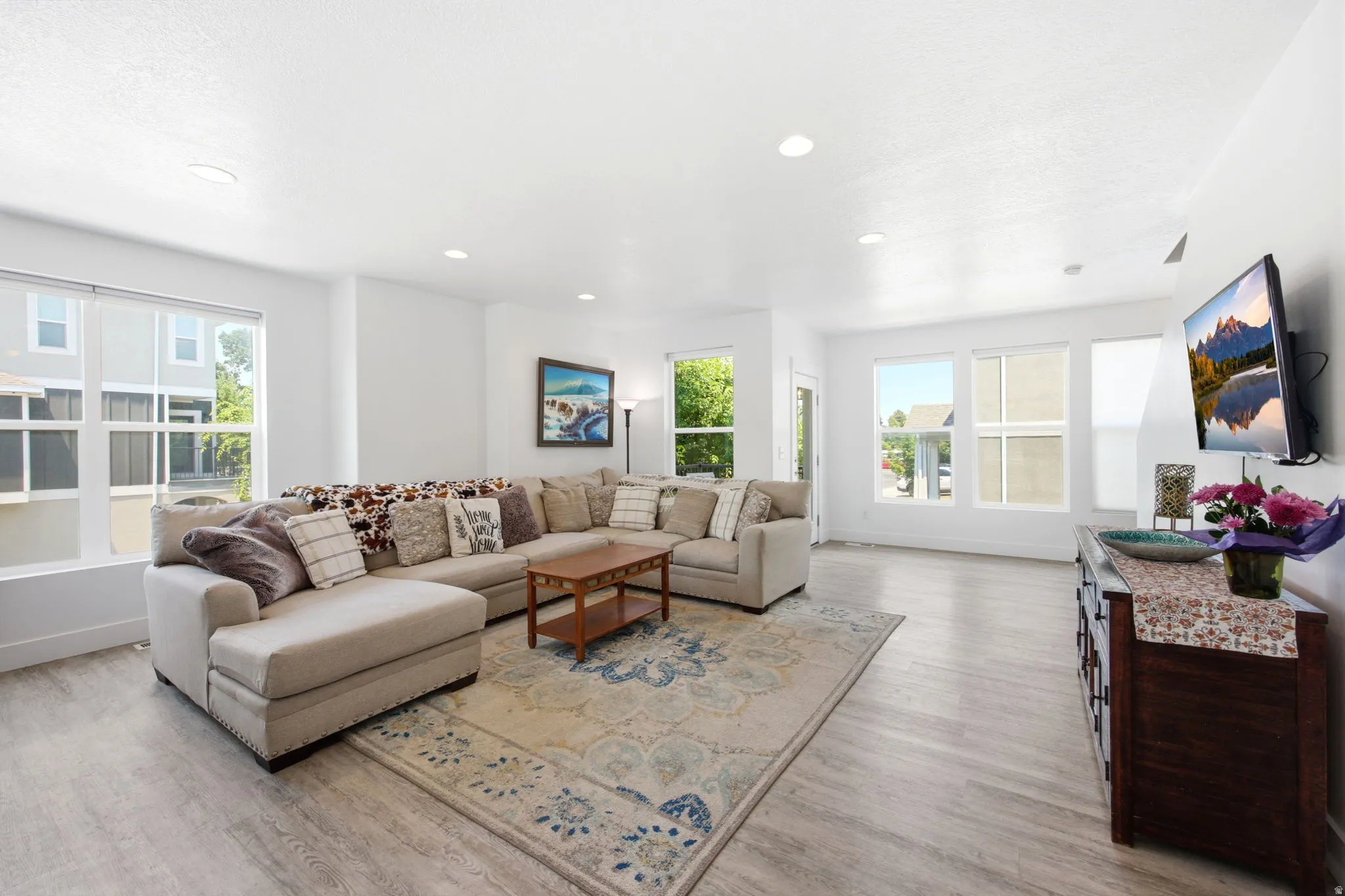 Spacious living area featuring light wood-finish flooring, numerous windows, recessed lighting, and a white color palette