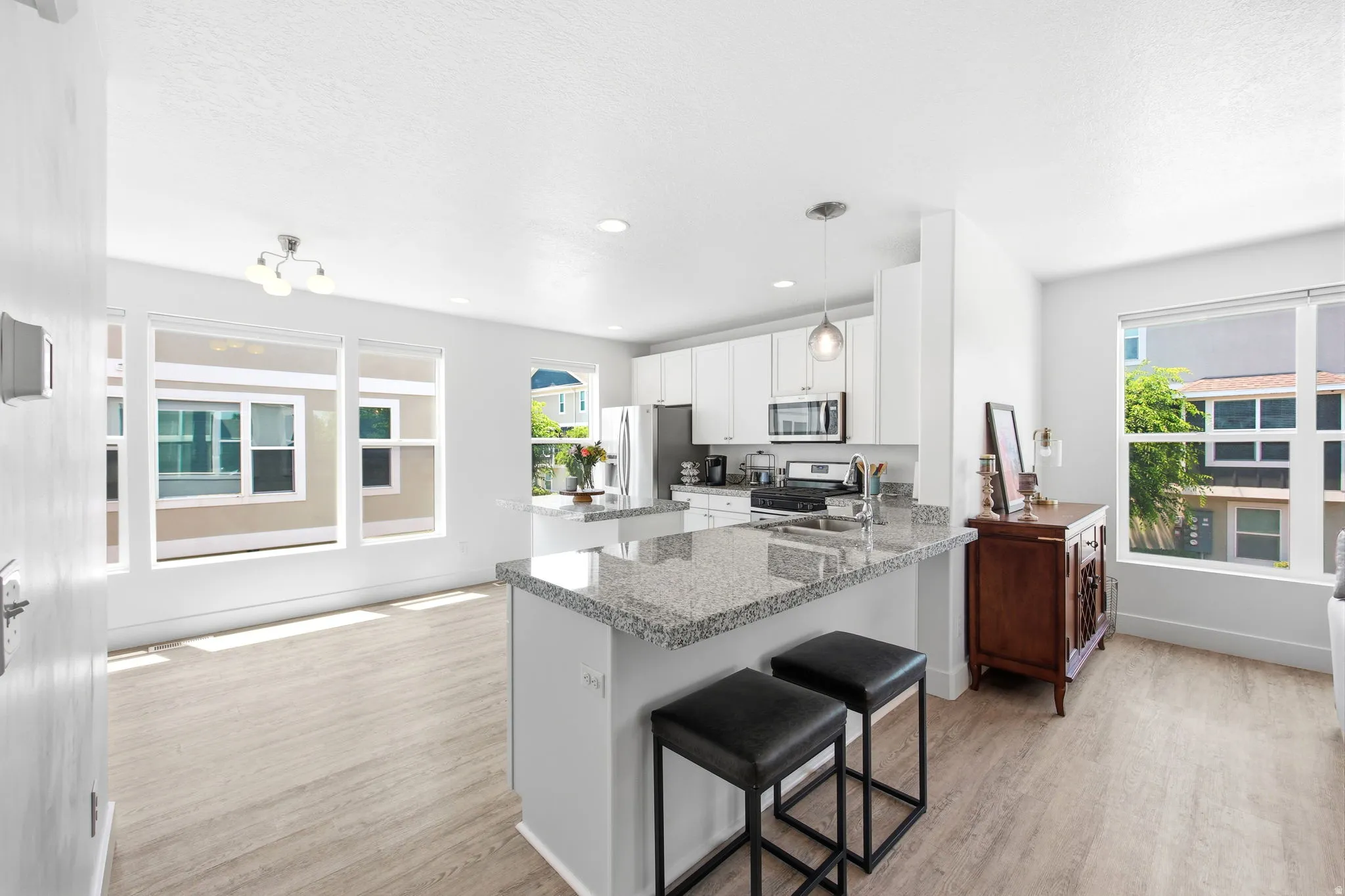 Open-concept kitchen with a large island featuring a light-toned granite countertop, white cabinetry, and stainless steel appliances