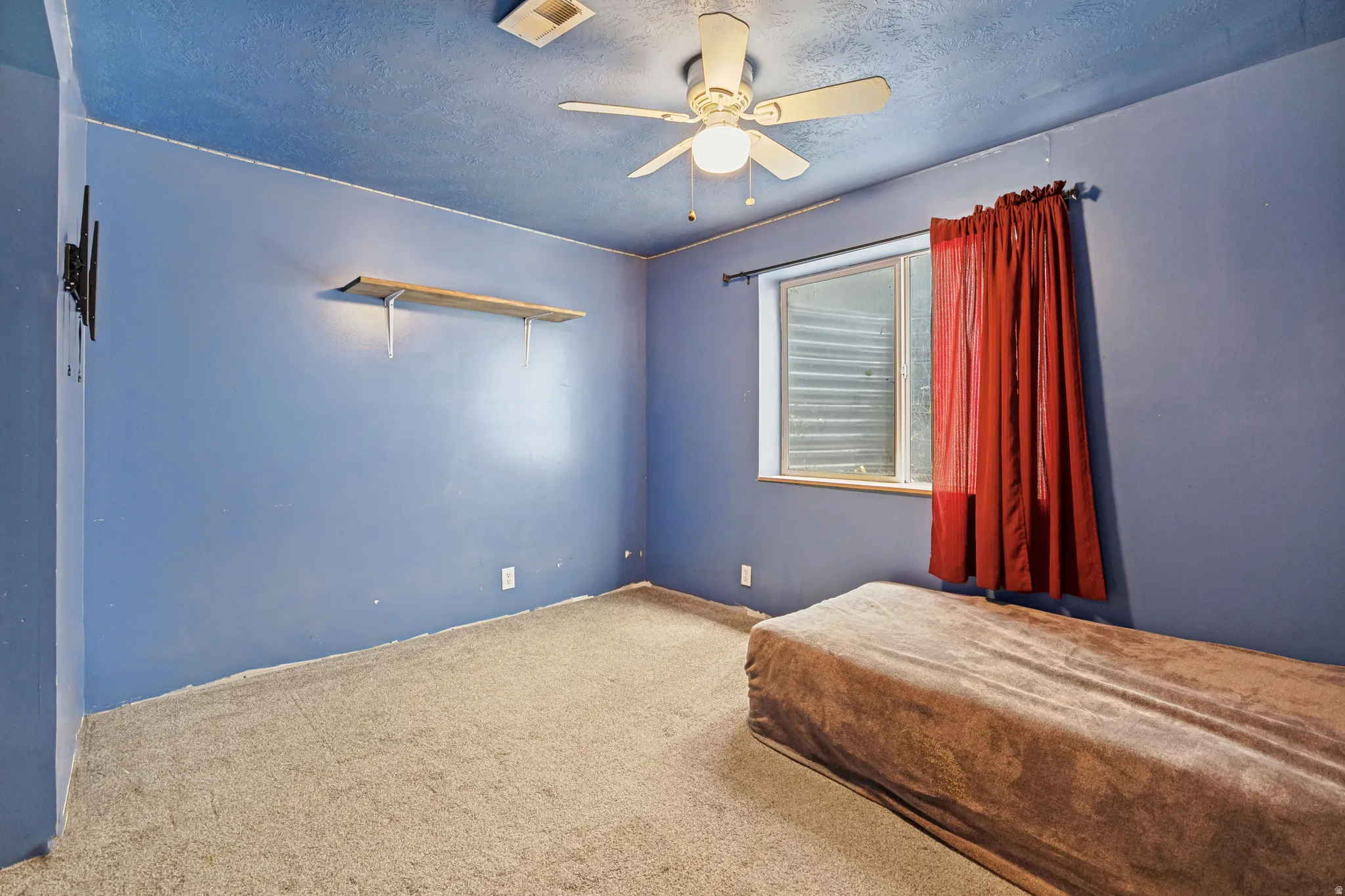 Carpeted interior space featuring a ceiling fan with integrated lighting, a window, and a wall-mounted shelf