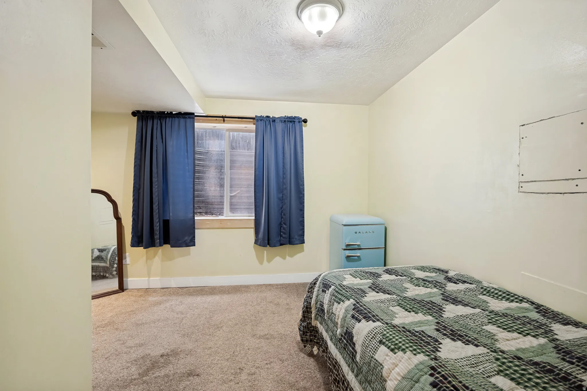 Carpeted room featuring a window with blue curtains and a ceiling-mounted light fixture