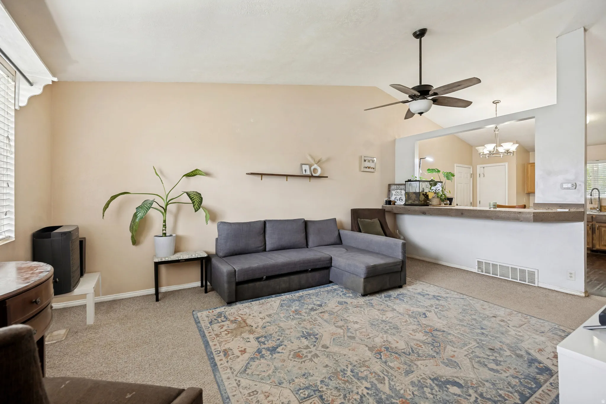 Living area featuring vaulted ceilings, a ceiling fan with integrated lighting, and carpet flooring
