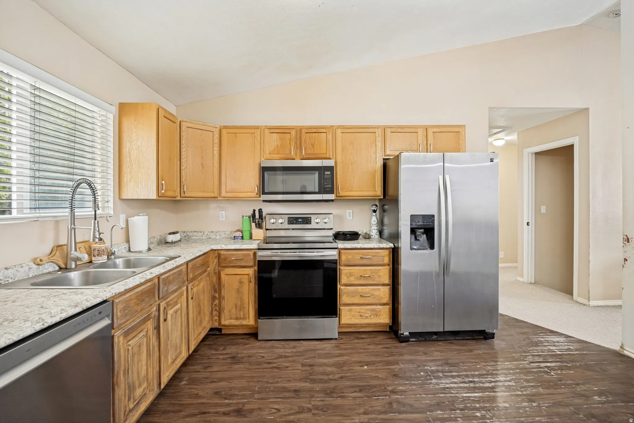 Kitchen featuring wood cabinetry, stainless steel appliances, a double basin sink, and wood-finish flooring