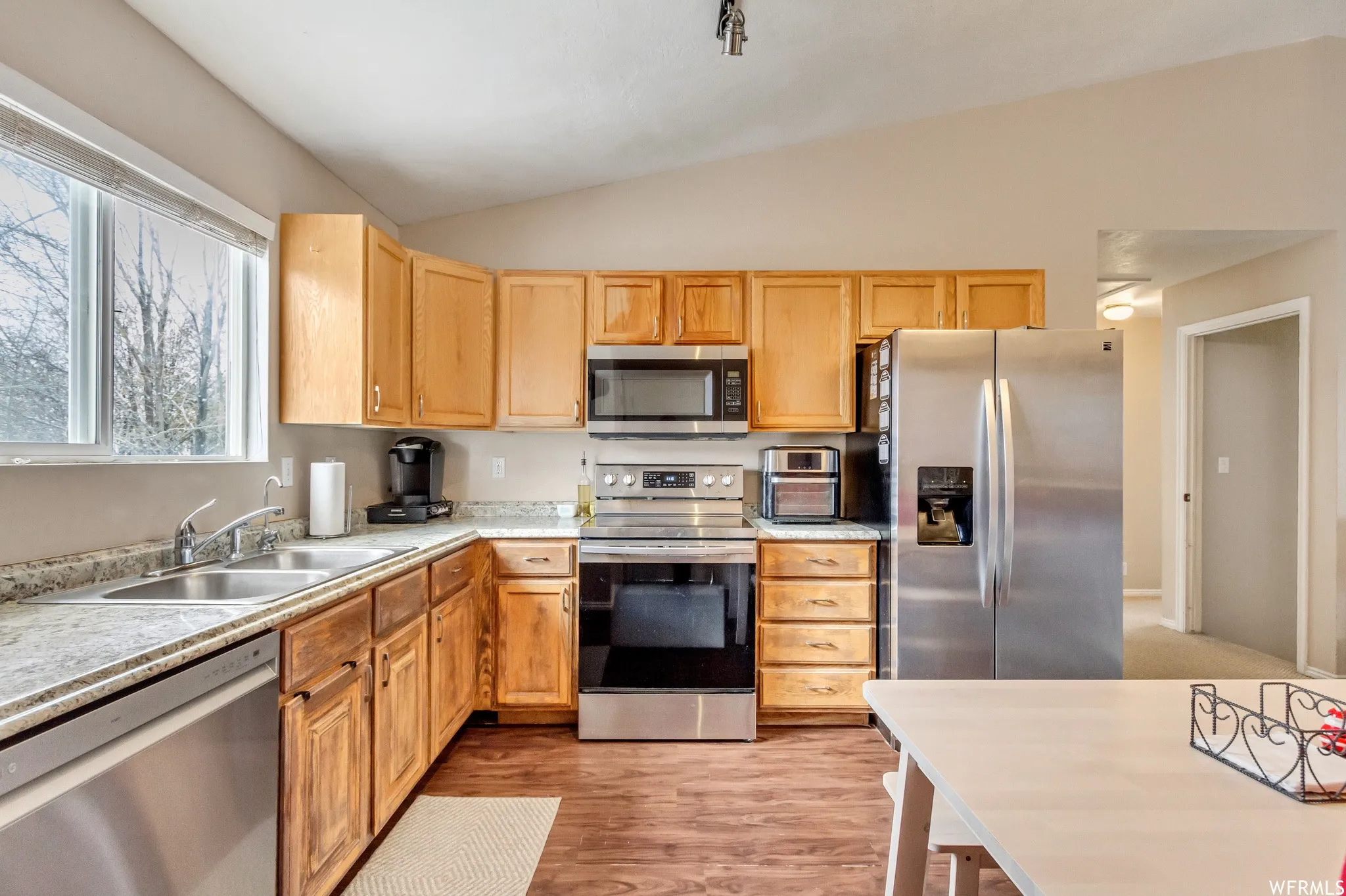 Kitchen featuring wood cabinetry, stainless steel appliances, speckled countertops, a double basin sink, and wood-finish flooring