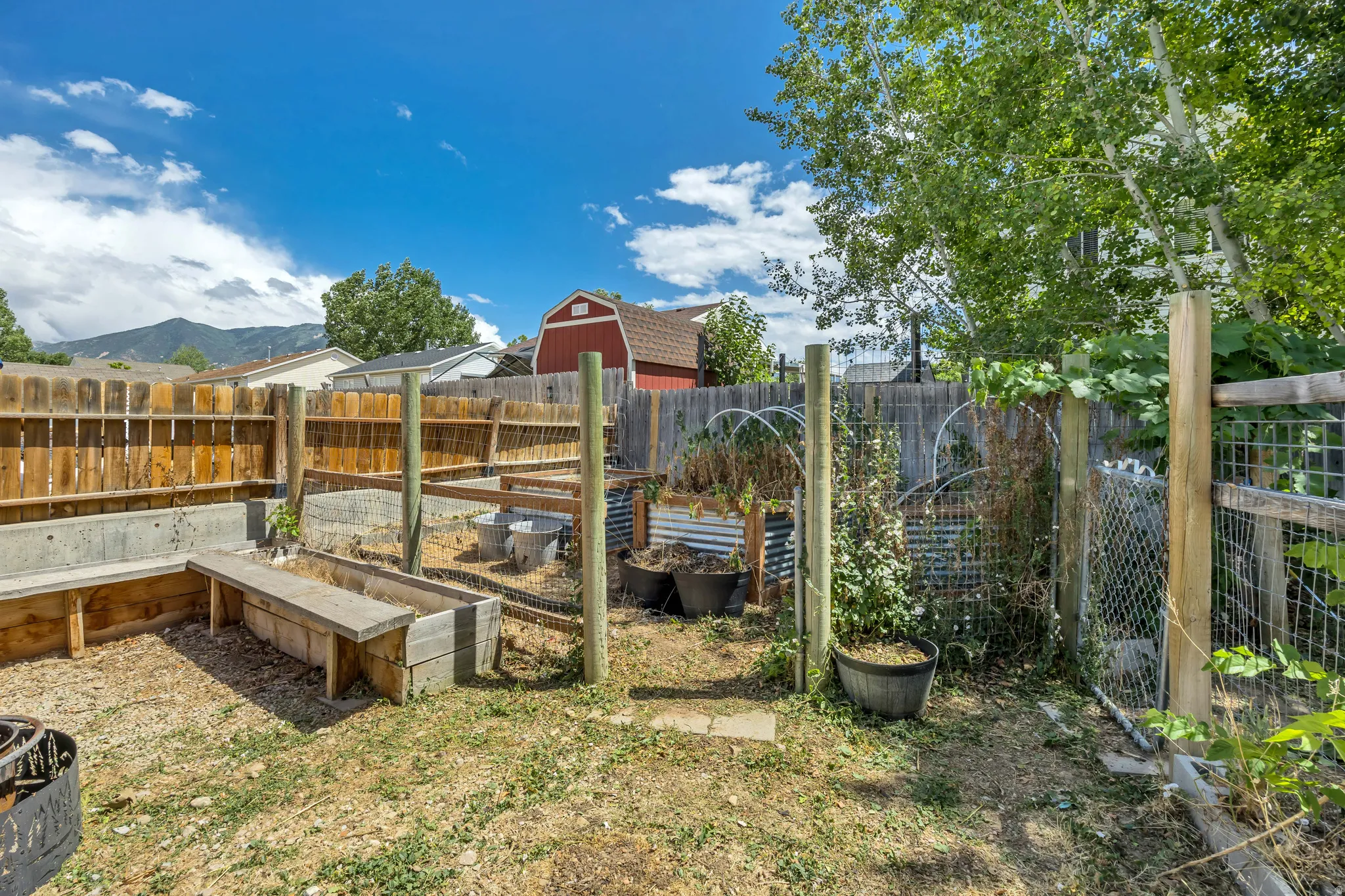 Fenced backyard featuring raised garden beds, a gravel patio area, and mature trees