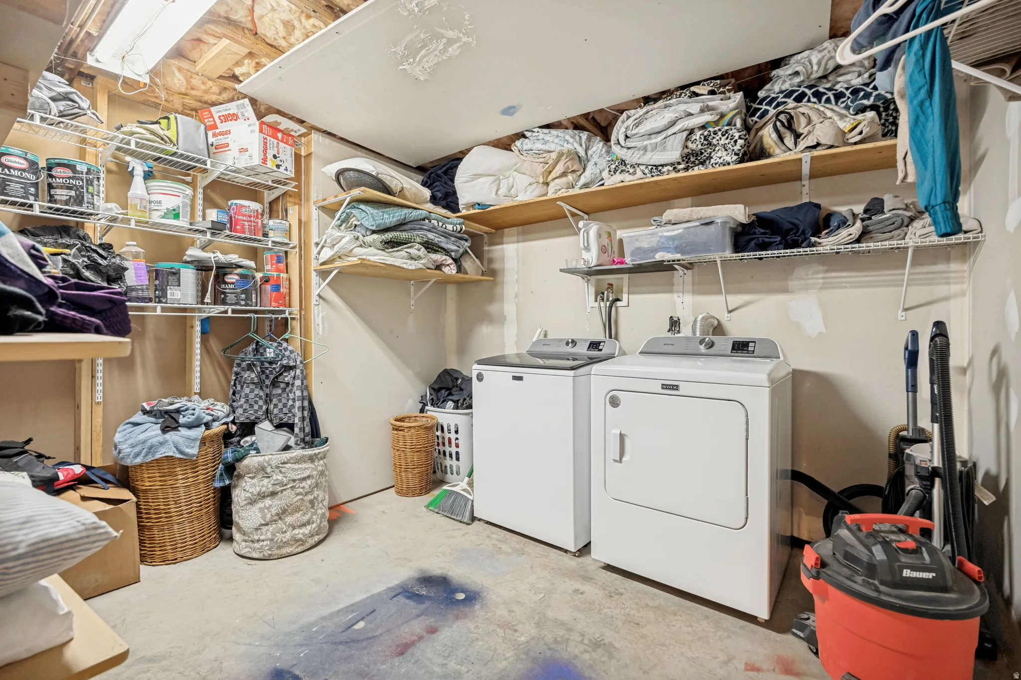 Dedicated laundry area featuring a washer and dryer, concrete flooring, and multiple wall-mounted shelving units for organization