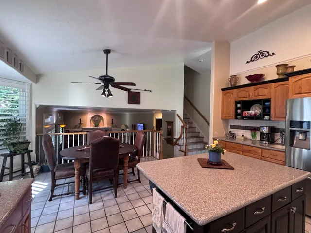 Kitchen and dining areas featuring a large center island with a speckled countertop, a stainless steel refrigerator, wood cabinetry, and a tile backsplash