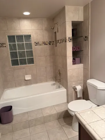 Bathroom featuring a tiled shower surround with glass block window and decorative stone-look accent banding