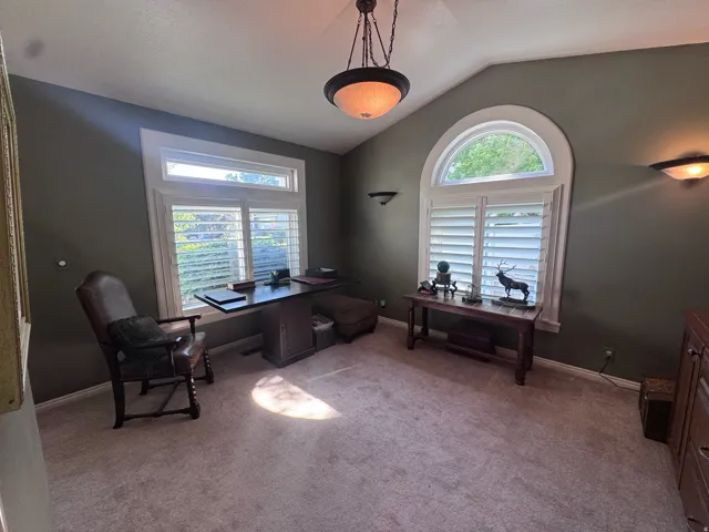 Vaulted ceiling room featuring a large arched window, an additional rectangular transom window, white plantation shutters, and recessed wall sconces