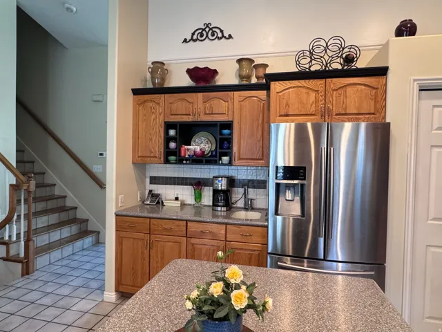 Kitchen featuring wood cabinetry, stainless steel French door refrigerator, speckled granite-style countertops, and a tiled backsplash