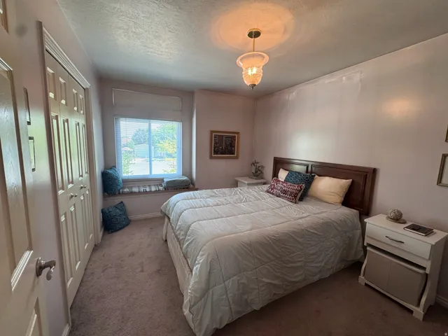 Carpeted interior space featuring a window with a built-in window seat, a wood-finish headboard, a ceiling-mounted light fixture, and bifold closet doors