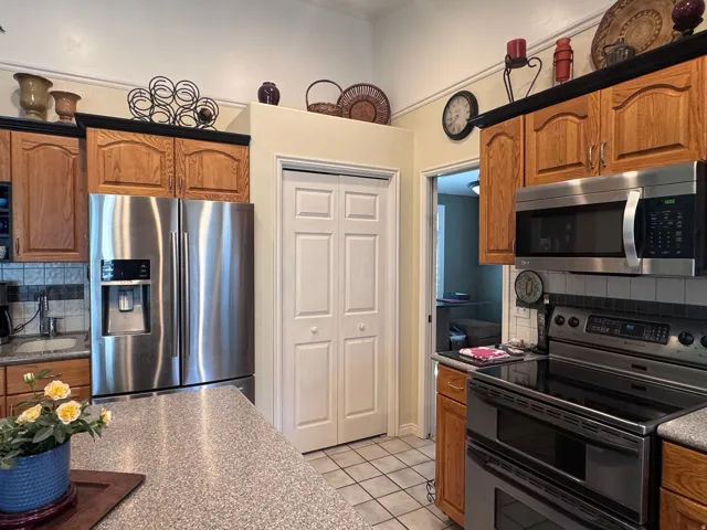 Kitchen featuring wood cabinetry with black trim, stainless steel appliances, a tile backsplash, and a light-colored countertop