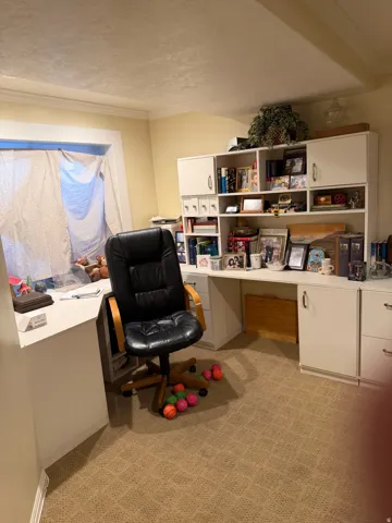 Built-in desk with overhead cabinetry and storage, featuring a window with natural light and a textured carpet flooring