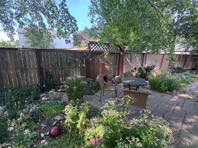 Stone paver patio featuring a bistro table and chairs, surrounded by mature plantings and a wood fence with lattice accents