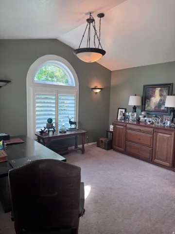 Vaulted ceiling room featuring an arched window with plantation shutters, a hanging bowl light fixture, and wall sconces