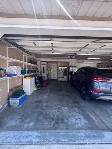 Attached garage with a concrete floor, overhead garage door, interior access door, and built-in shelving