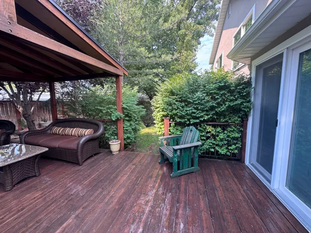 Expansive outdoor deck featuring wood flooring, a covered patio structure, and dense perimeter landscaping