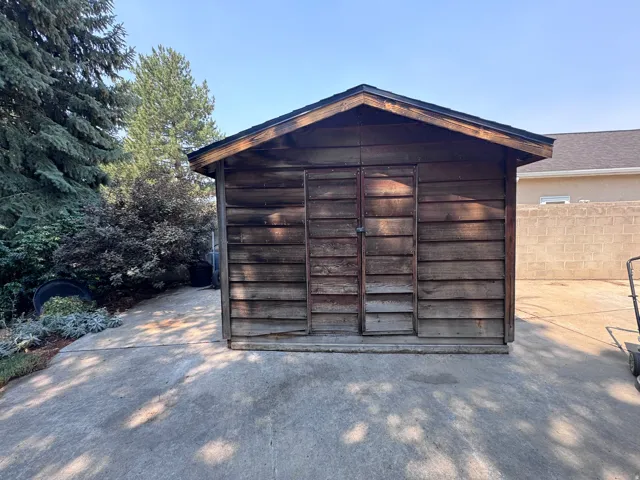 Wood-sided storage shed with a gabled roof, featuring double doors and set on a concrete pad